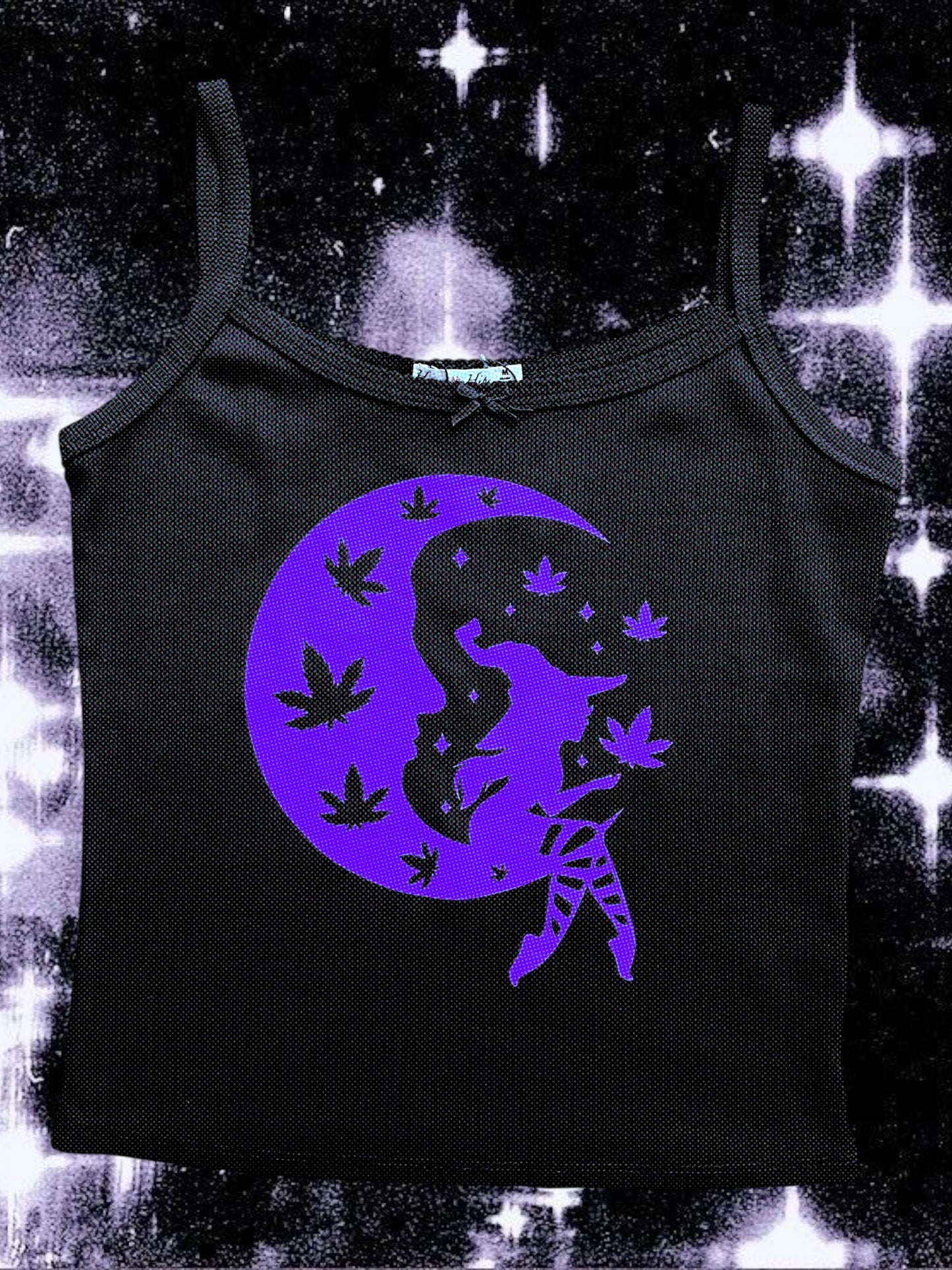 Black spaghetti strap tank top with a purple print of a seated witch on a crescent moon, surrounded by floating cannabis leaves and stars. The background is a cosmic, sparkly black-and-white space scene.
