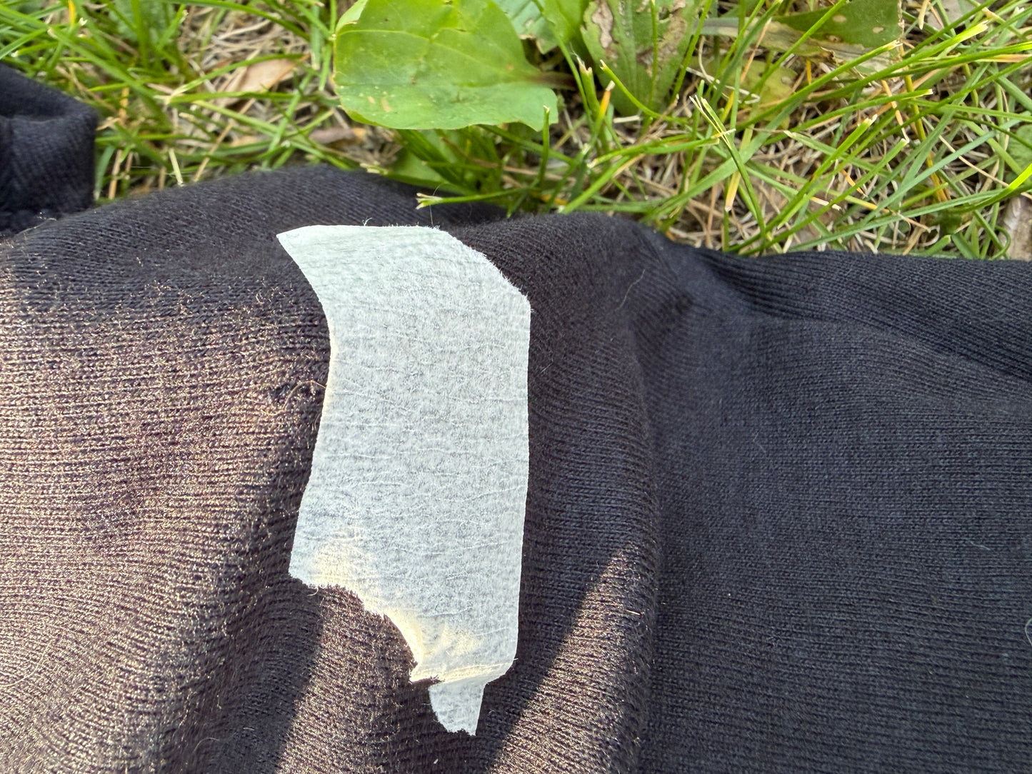 A piece of white tape is stuck to a black fabric, partially covering a small tear in the fabric.