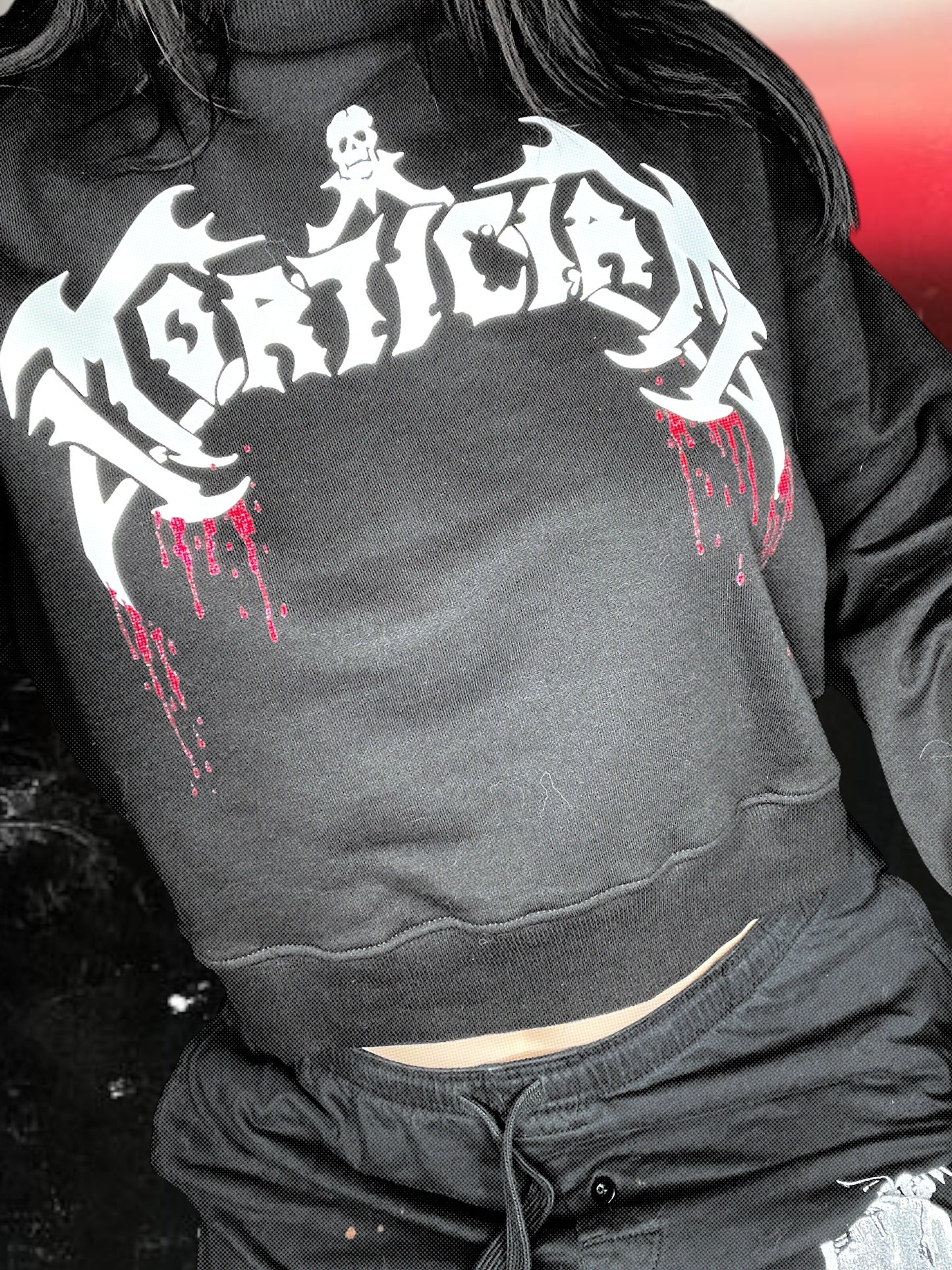 A person wearing a black sweatshirt with a graphic design featuring a skull and crossbones symbol.