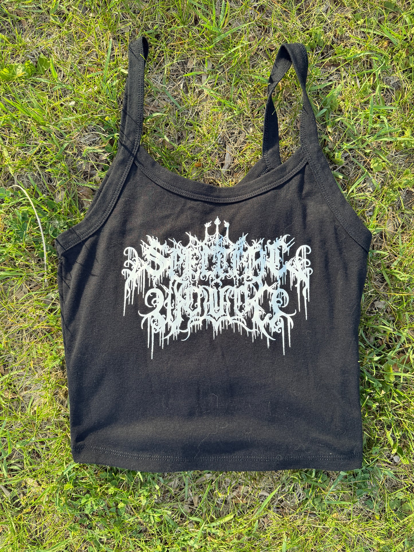A black crop top with white text printed on it, lying on a grassy surface.