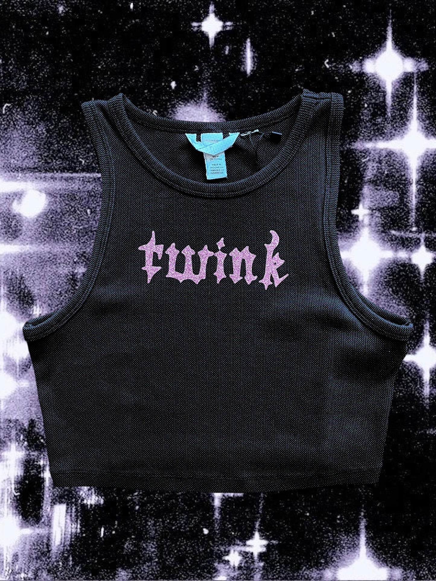 Black ribbed cropped tank top with pink glitter gothic text that reads “twink” across the chest. Shirt is laid flat against a black-and-white cosmic starry background.