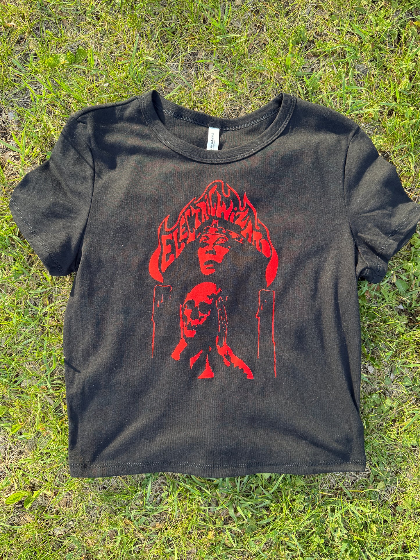 a black t-shirt with a red graphic design on it, lying on a grassy surface.