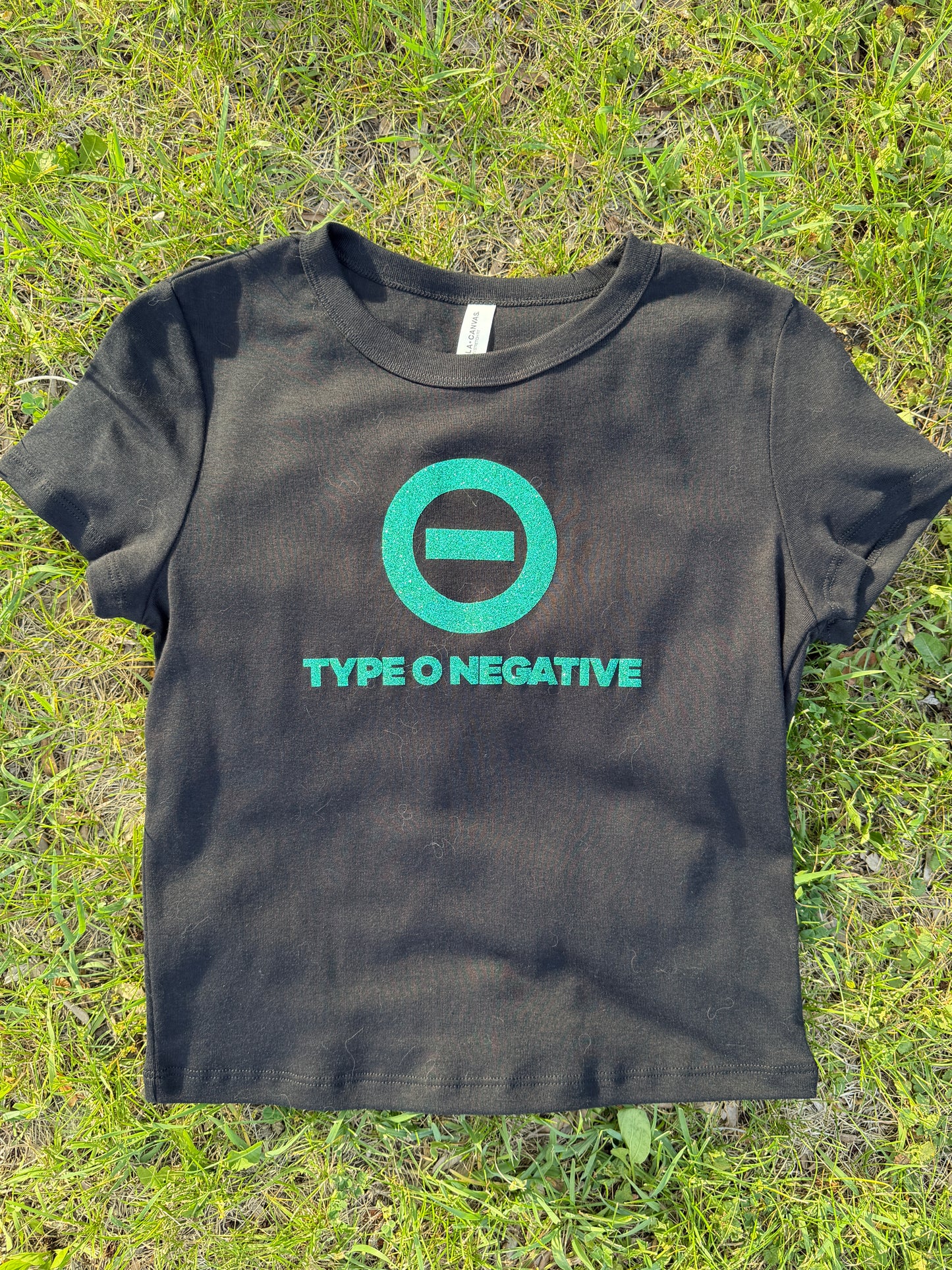 A black t-shirt with a green logo and text printed on it, lying on a grassy surface.