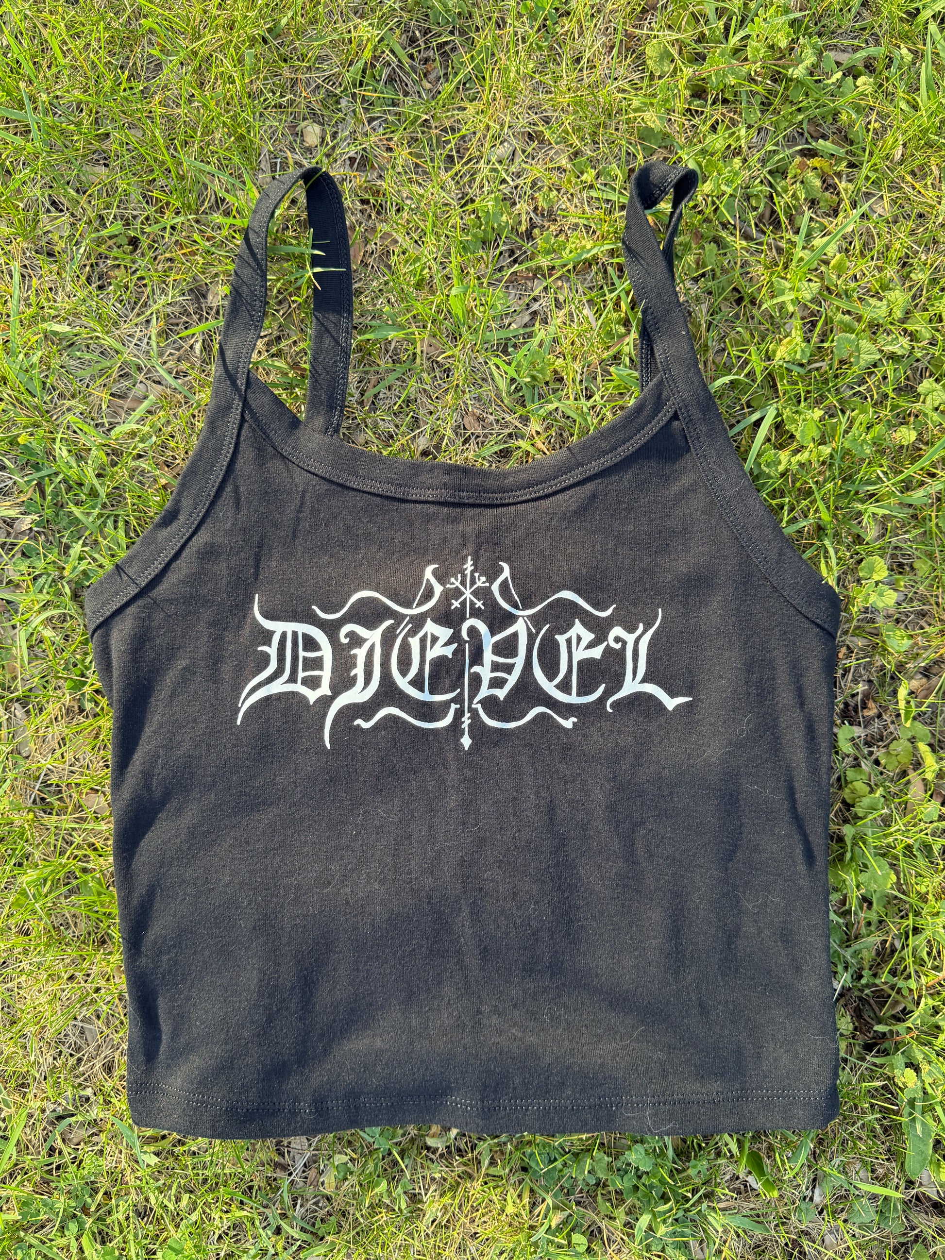 A black tank top with white text printed on it, lying on a grassy surface.