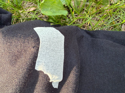 A piece of white tape is stuck to a black fabric, partially covering a small tear in the fabric.