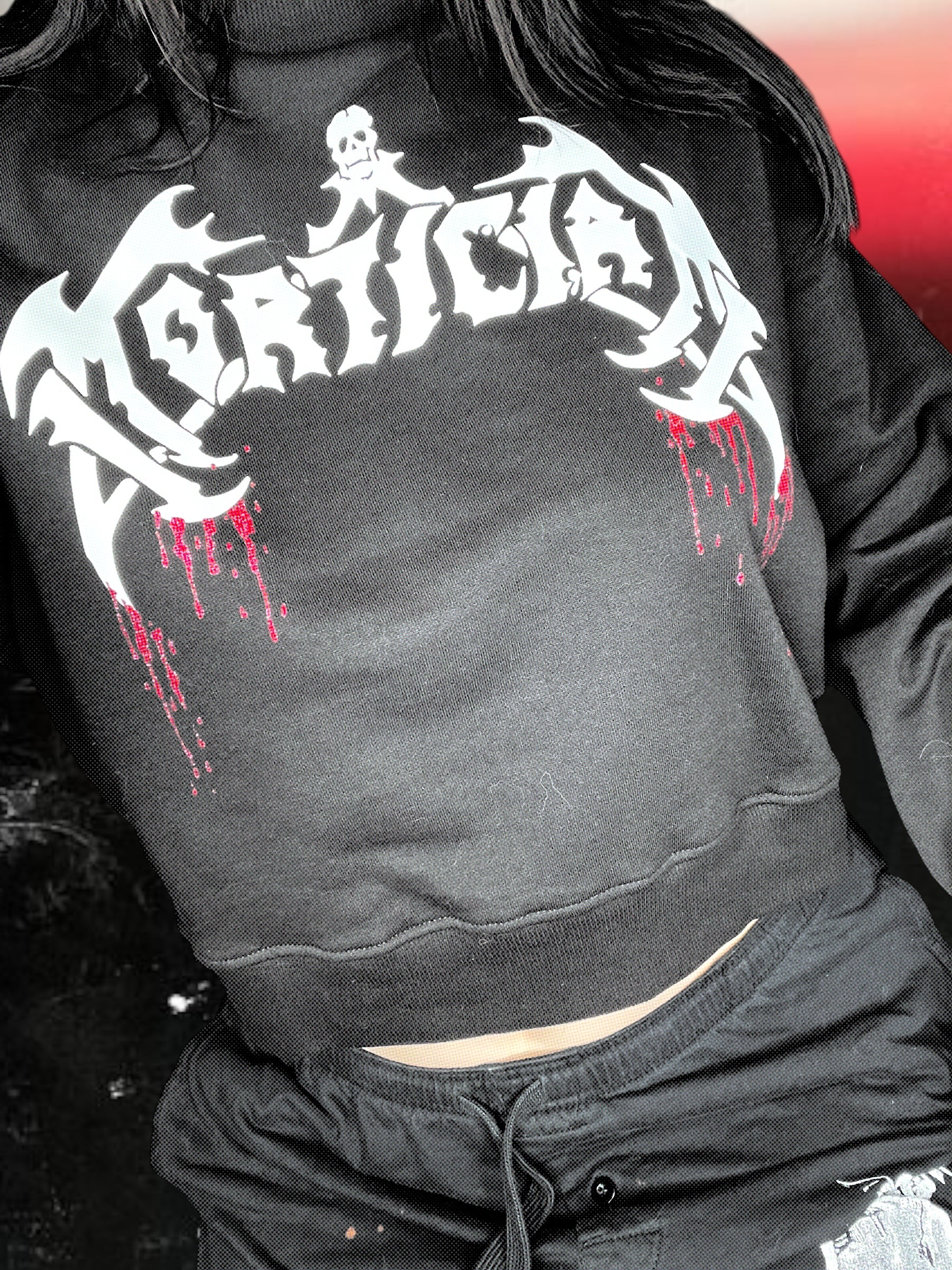 A person wearing a black sweatshirt with a graphic design featuring a skull and crossbones symbol.