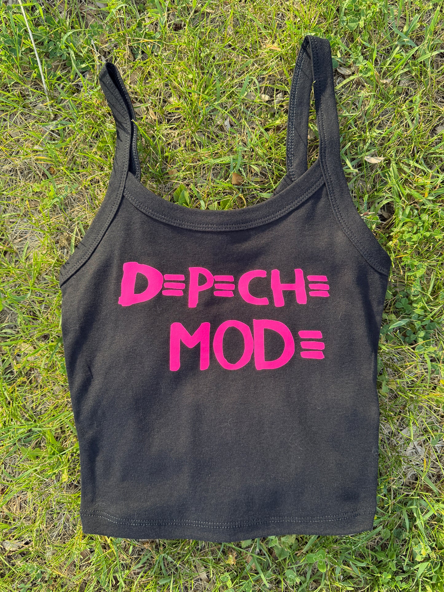 A black crop top with pink text printed on it, lying on a grassy surface.