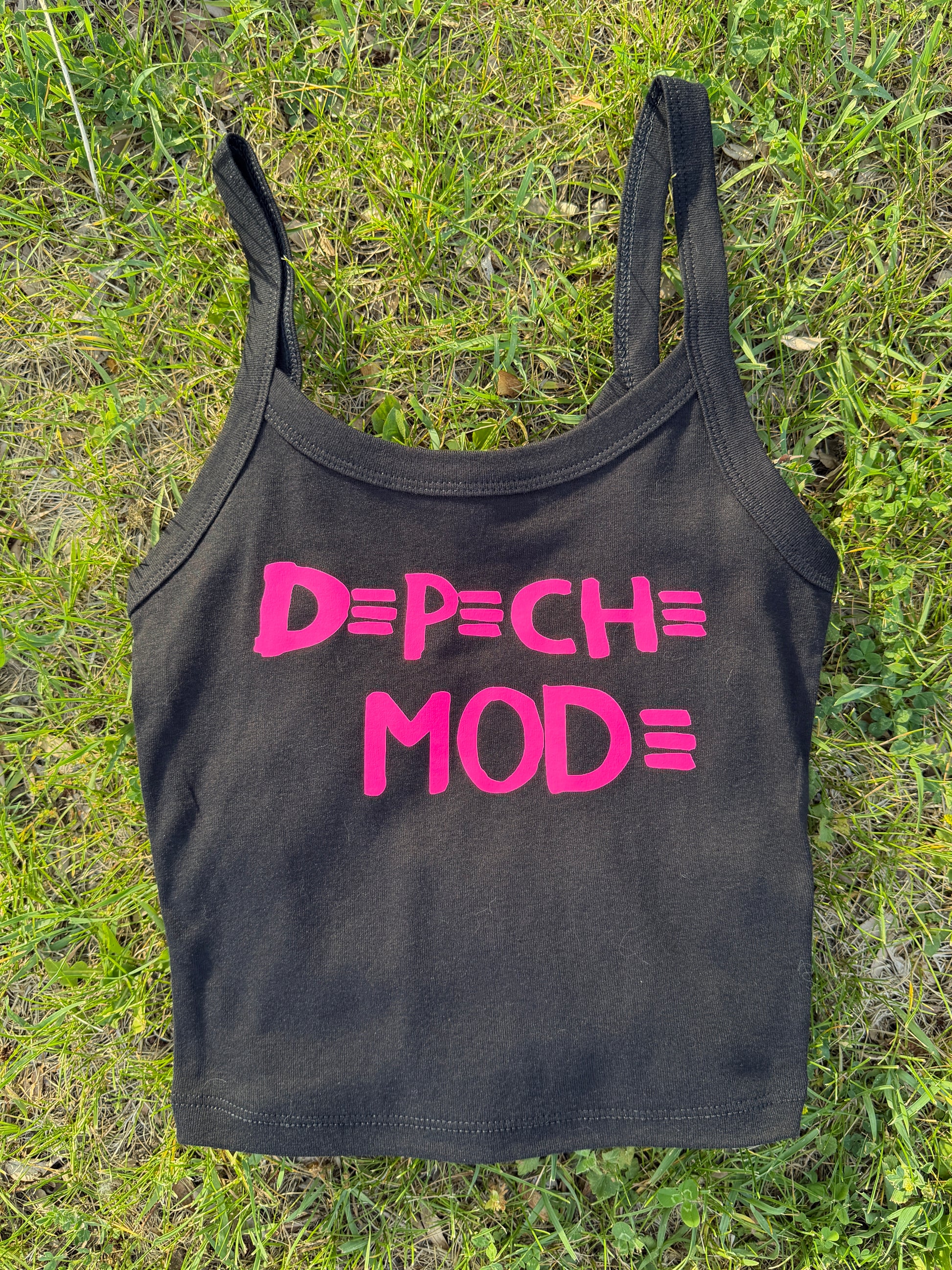 A black crop top with pink text printed on it, lying on a grassy surface.