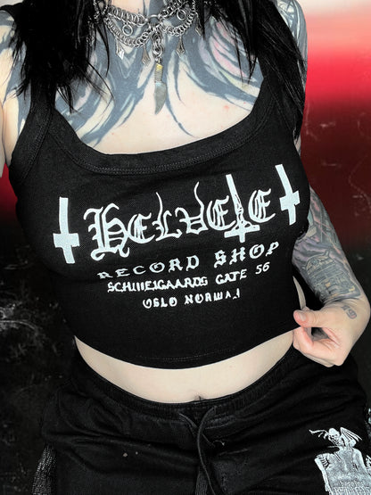 Black cropped spaghetti strap cami with “Helvete Record Shop” printed in white glitter vinyl. The design includes gothic text, upside-down crosses, and the address "Schweigaards Gate 56, Oslo Norway." Shirt is laid flat on a cosmic black-and-white starry background.