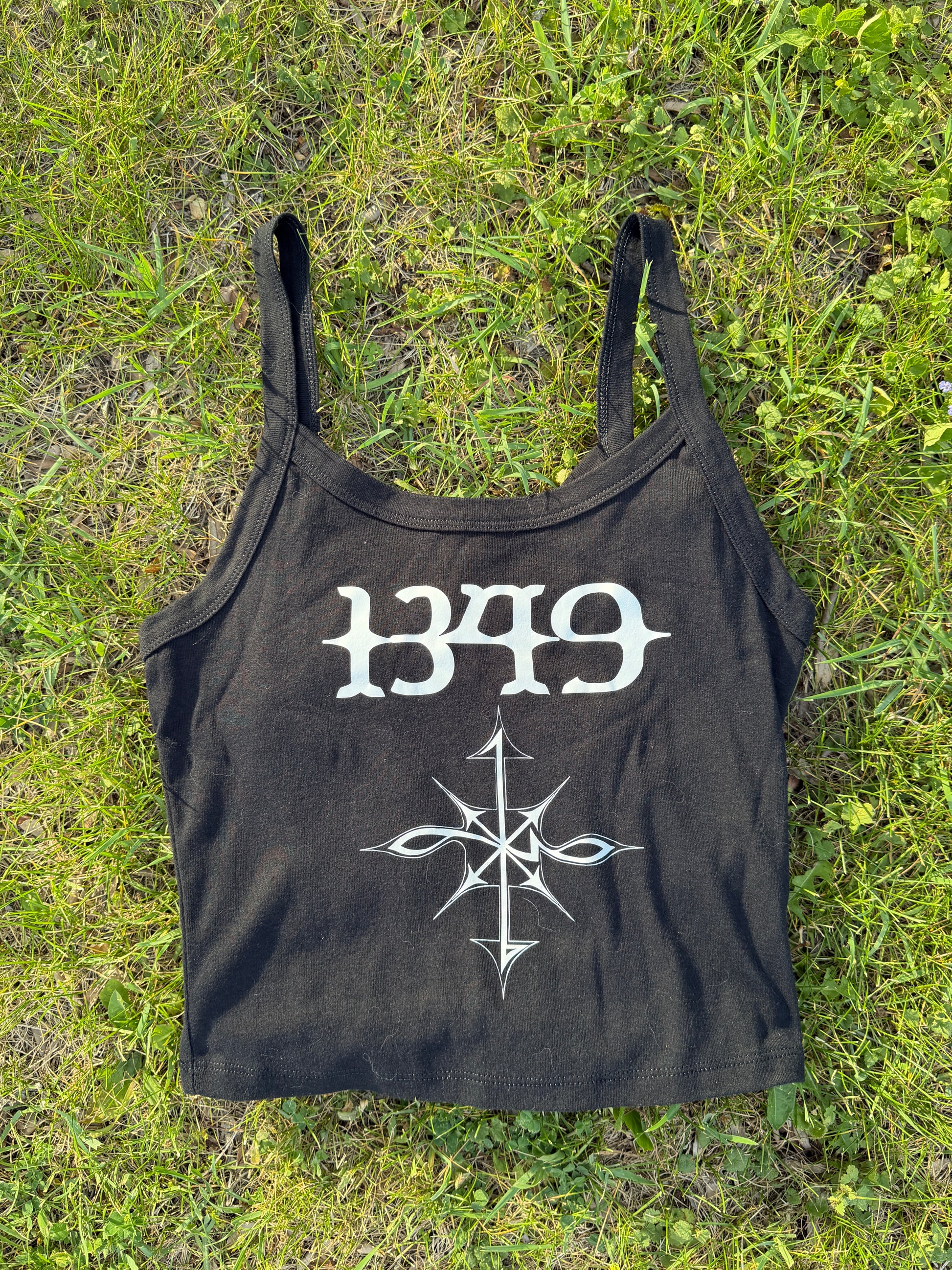 A black tank top with white text and a graphic design is lying on the grass.