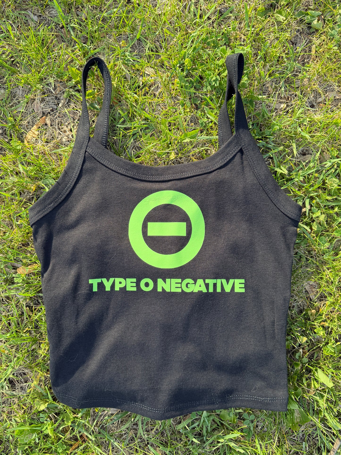 A black tank top with a green logo and text printed on it, lying on a grassy surface.