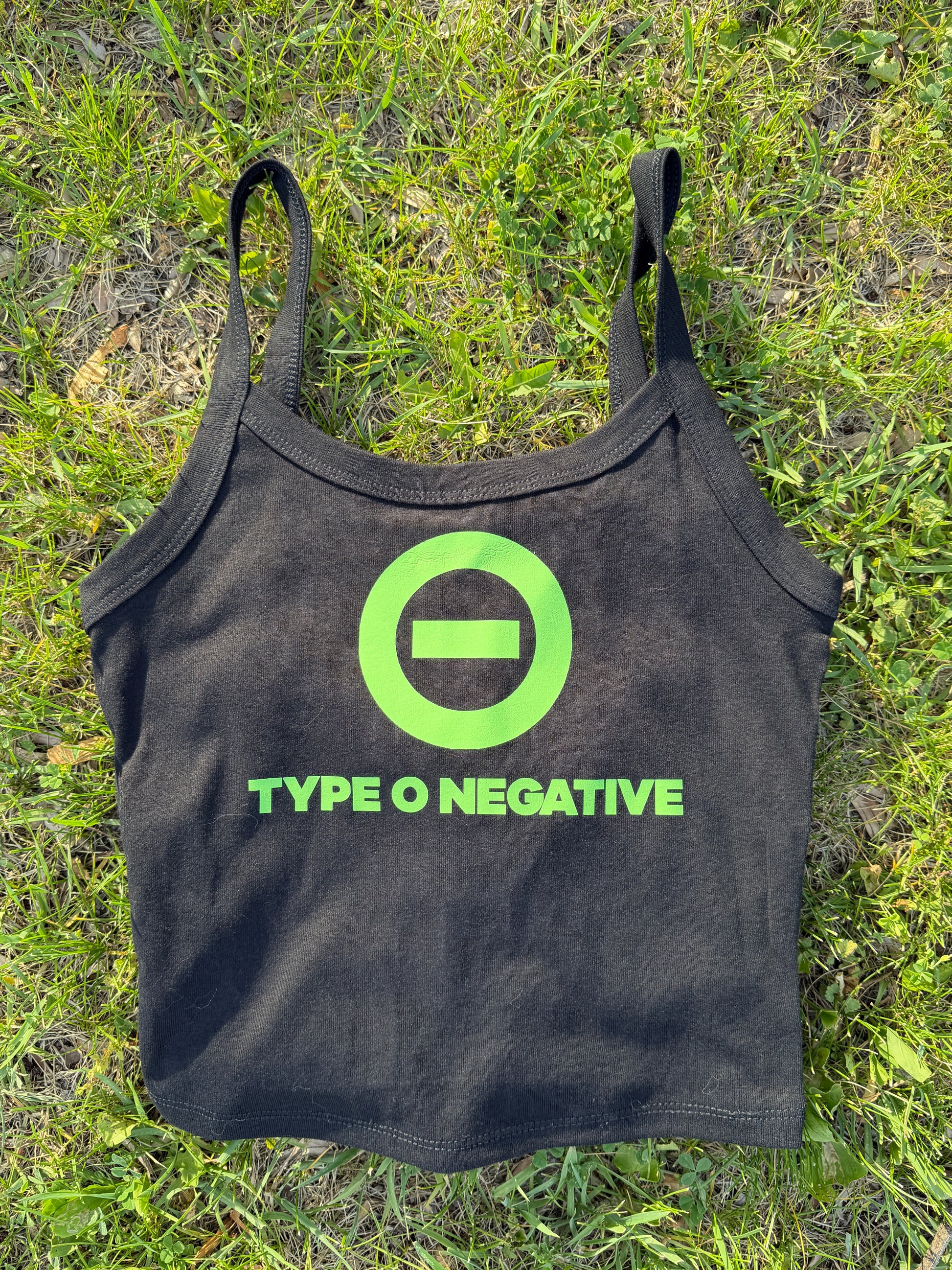 A black tank top with a green logo and text printed on it, lying on a grassy surface.