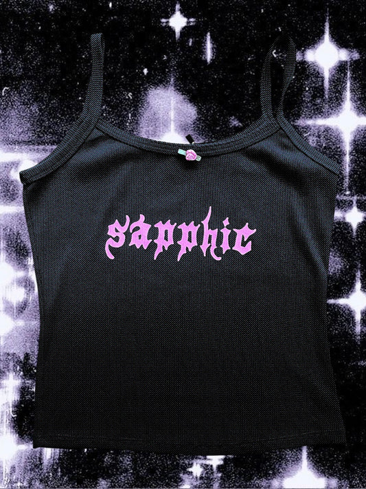 Black cropped spaghetti strap tank top with light pink gothic lettering that reads “sapphic” across the chest. The top has a small rose bow sewn at the neckline and is laid flat against a cosmic black-and-white starry background.