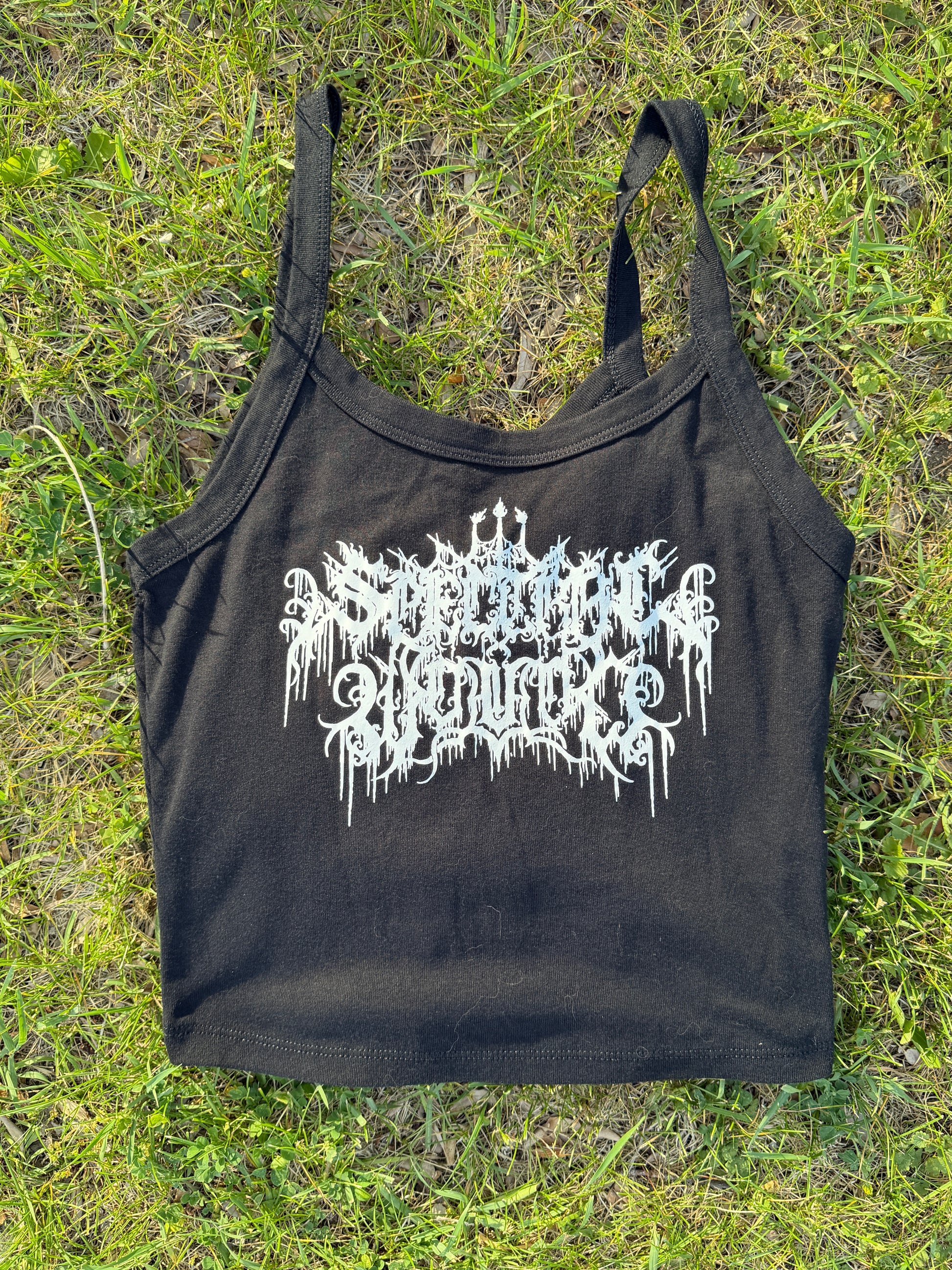 A black crop top with white text printed on it, lying on a grassy surface.