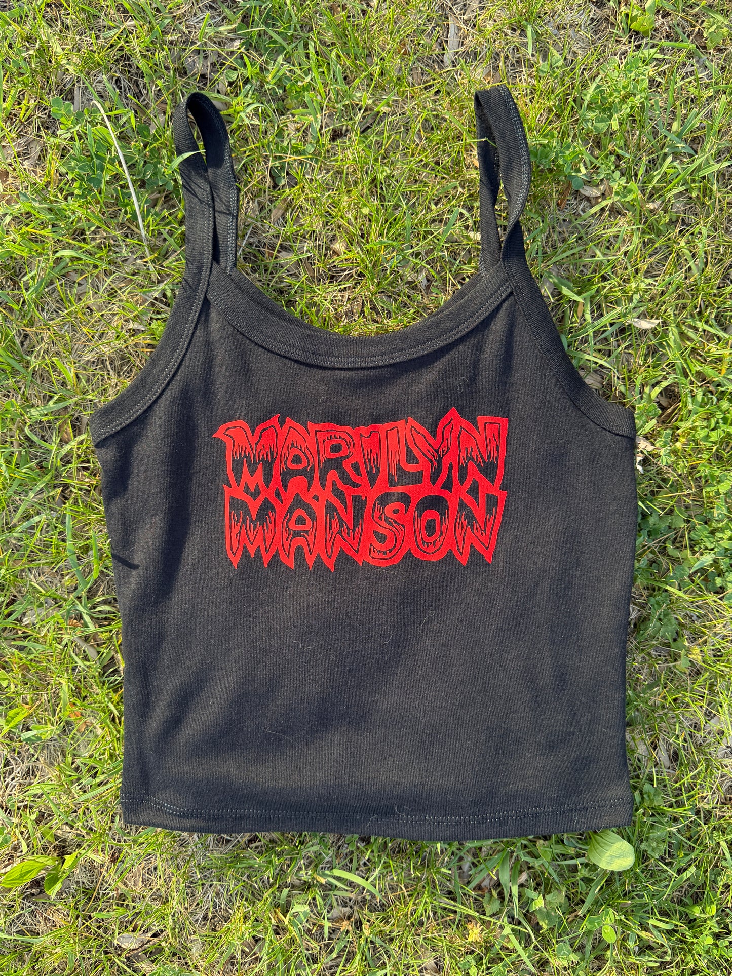 A black crop top with red text printed on it, lying on a grassy surface.