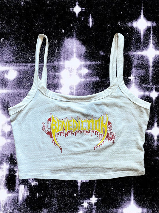 White cropped tank top with spaghetti straps featuring a yellow and red Benediction band logo in a death metal style, with cartoon monks holding crosses on each side. The shirt is laid flat on a starry black-and-white cosmic background.