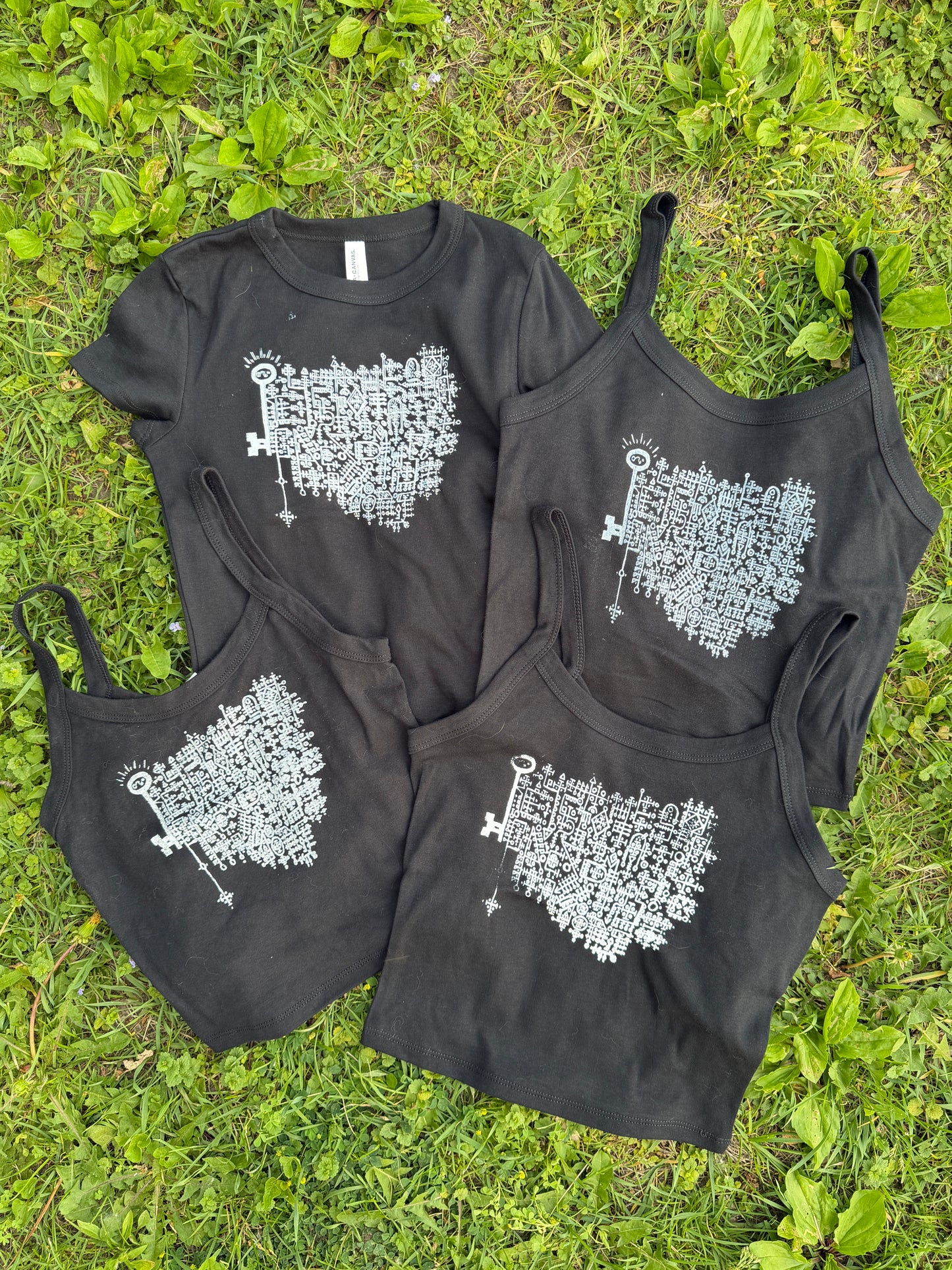 a collection of black t-shirts and tank tops lying on a grassy surface.