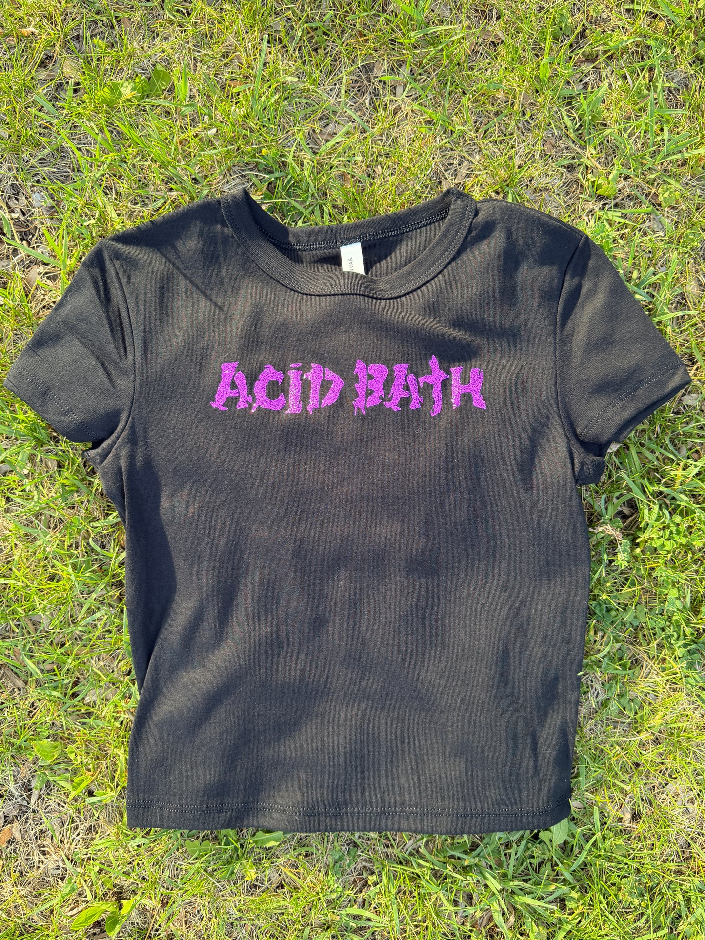 A black t-shirt with purple text printed on it, lying on a grassy surface.