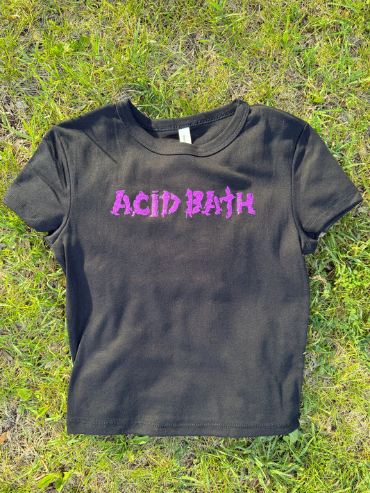 A black t-shirt with purple text printed on it, lying on a grassy surface.