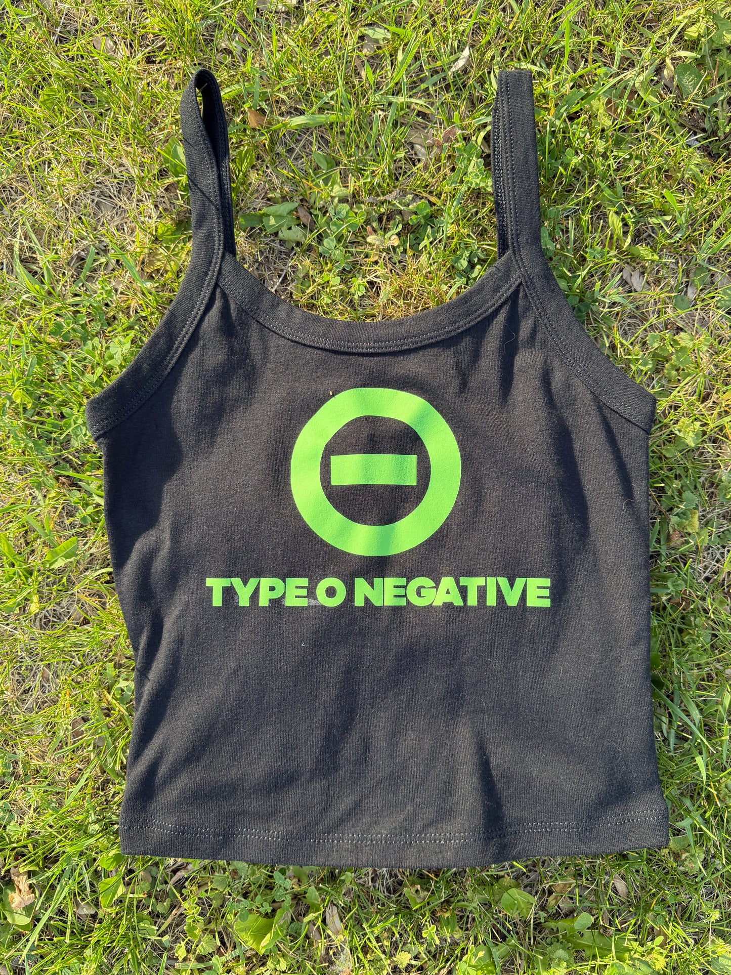 a black crop top with a green logo on it, lying on a grassy surface.