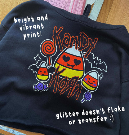 a black sweatshirt with a Halloween-themed design, including a candy corn, bats, and a bat-like character. The text on the sweatshirt reads "bright and vibrant print! Kandy Korn" and "glitter doesn'tflake or transfer ;)"