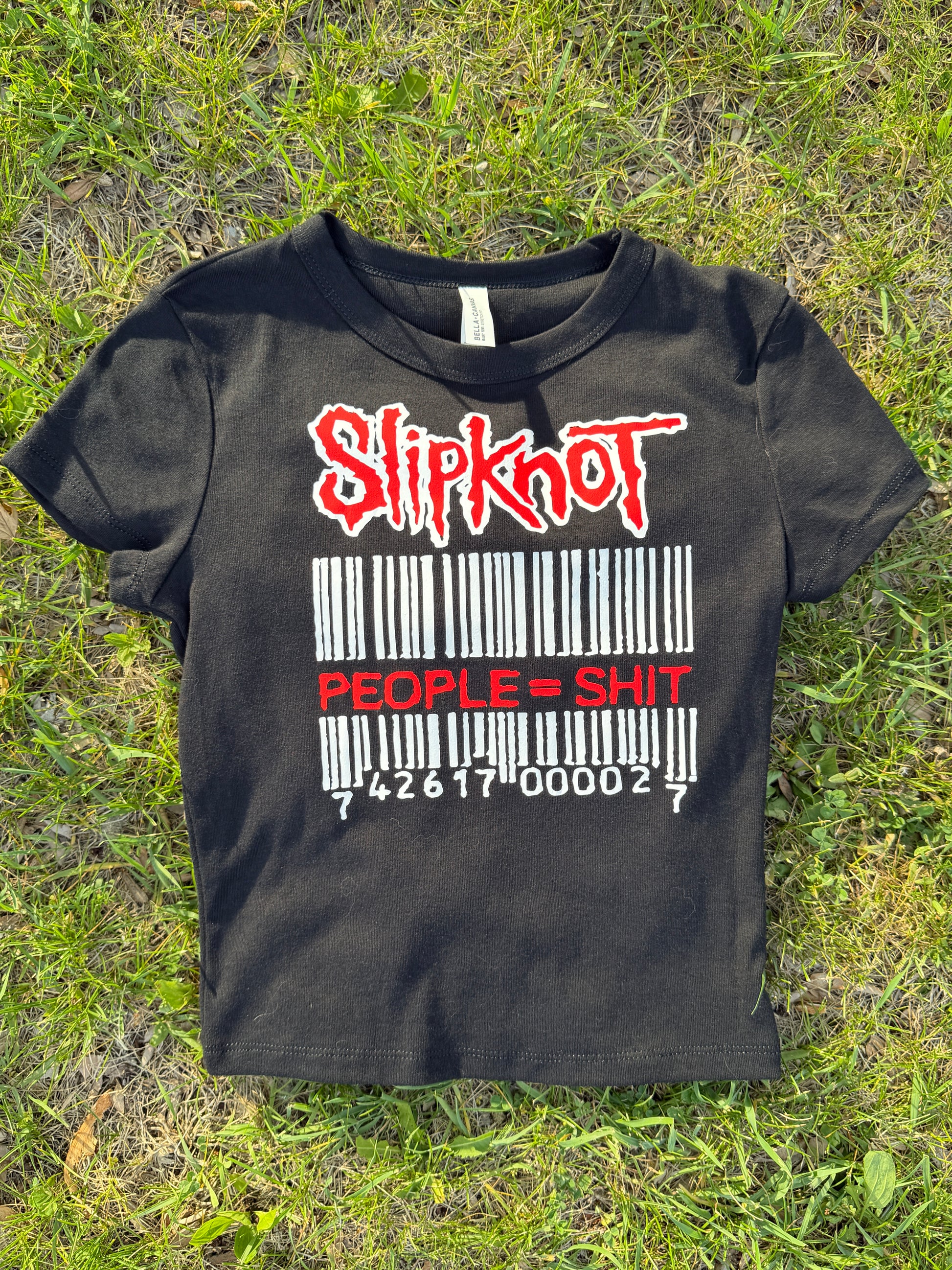 A black t-shirt with a graphic design printed on it, lying on the grass.