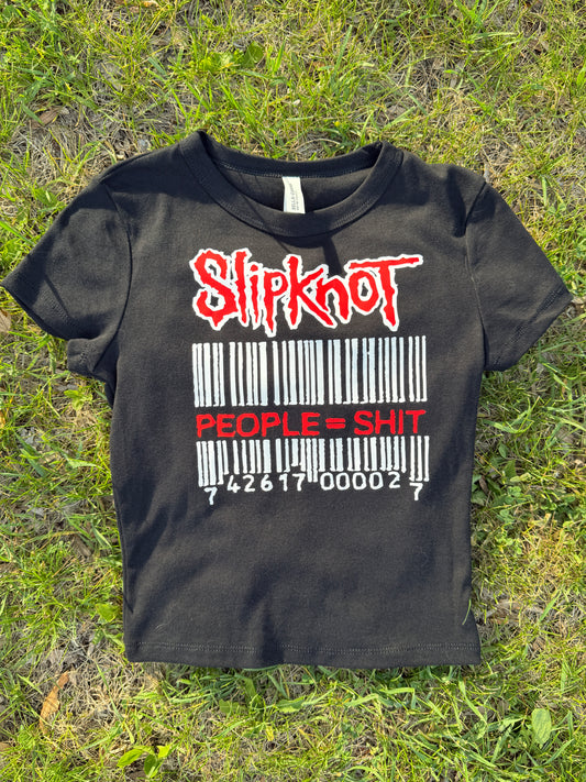 A black t-shirt with a graphic design printed on it, lying on the grass.