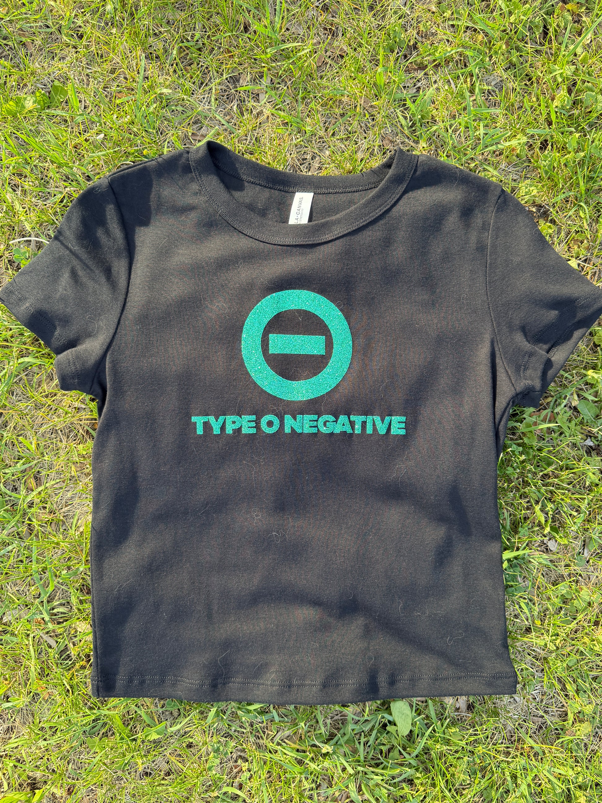 A black t-shirt with a green logo and text printed on it, lying on a grassy surface.